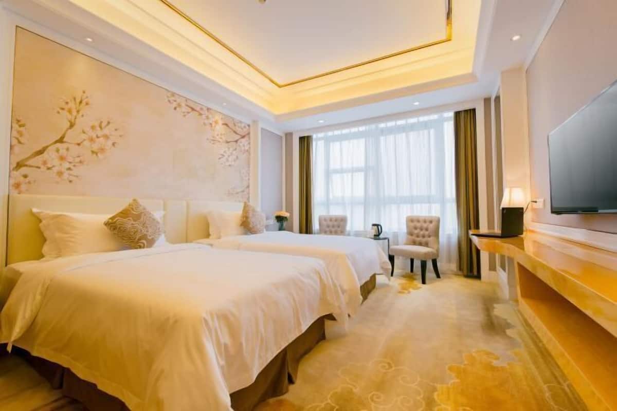 A hotel room with two beds, a large window with curtains, a flat-screen TV, and a decorative wall painting.
