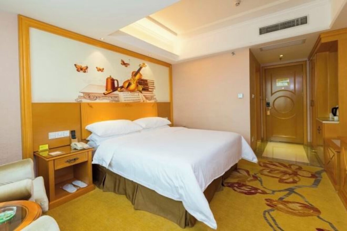 Ein Hotelzimmer mit Bett, Nachttisch, Sessel, Schreibtisch und einer Wand mit dekorativem Design.