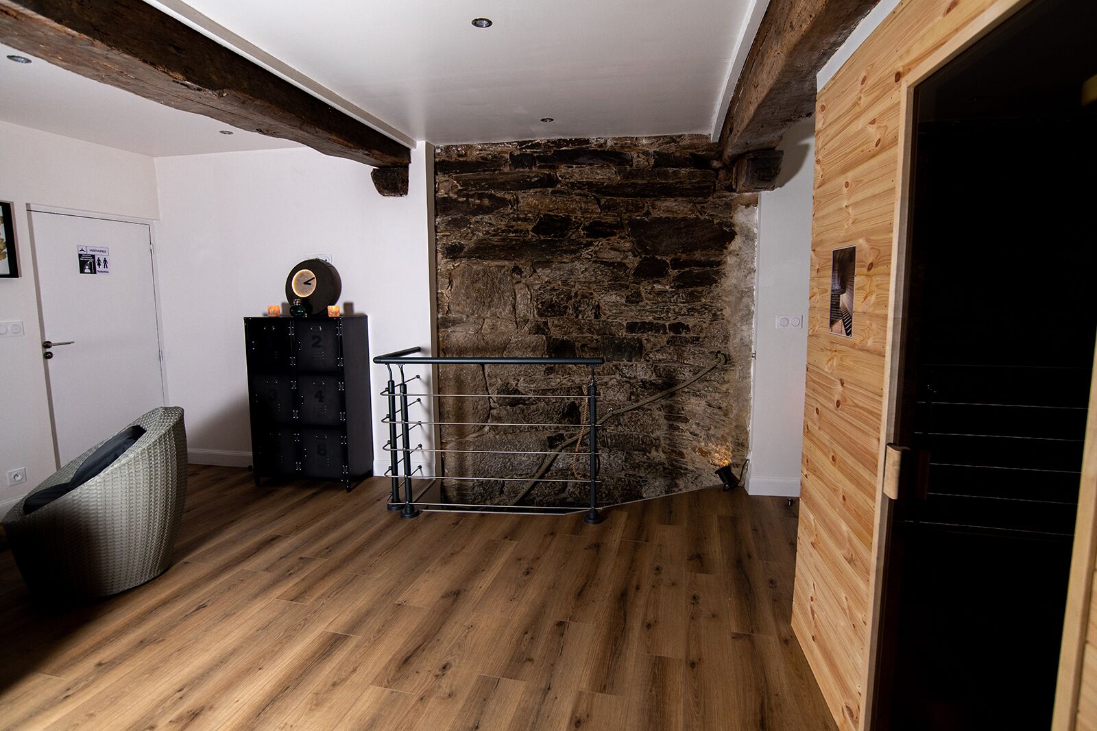 Une pièce avec un mur en pierre, des poutres en bois, un étagère en métal et une porte.