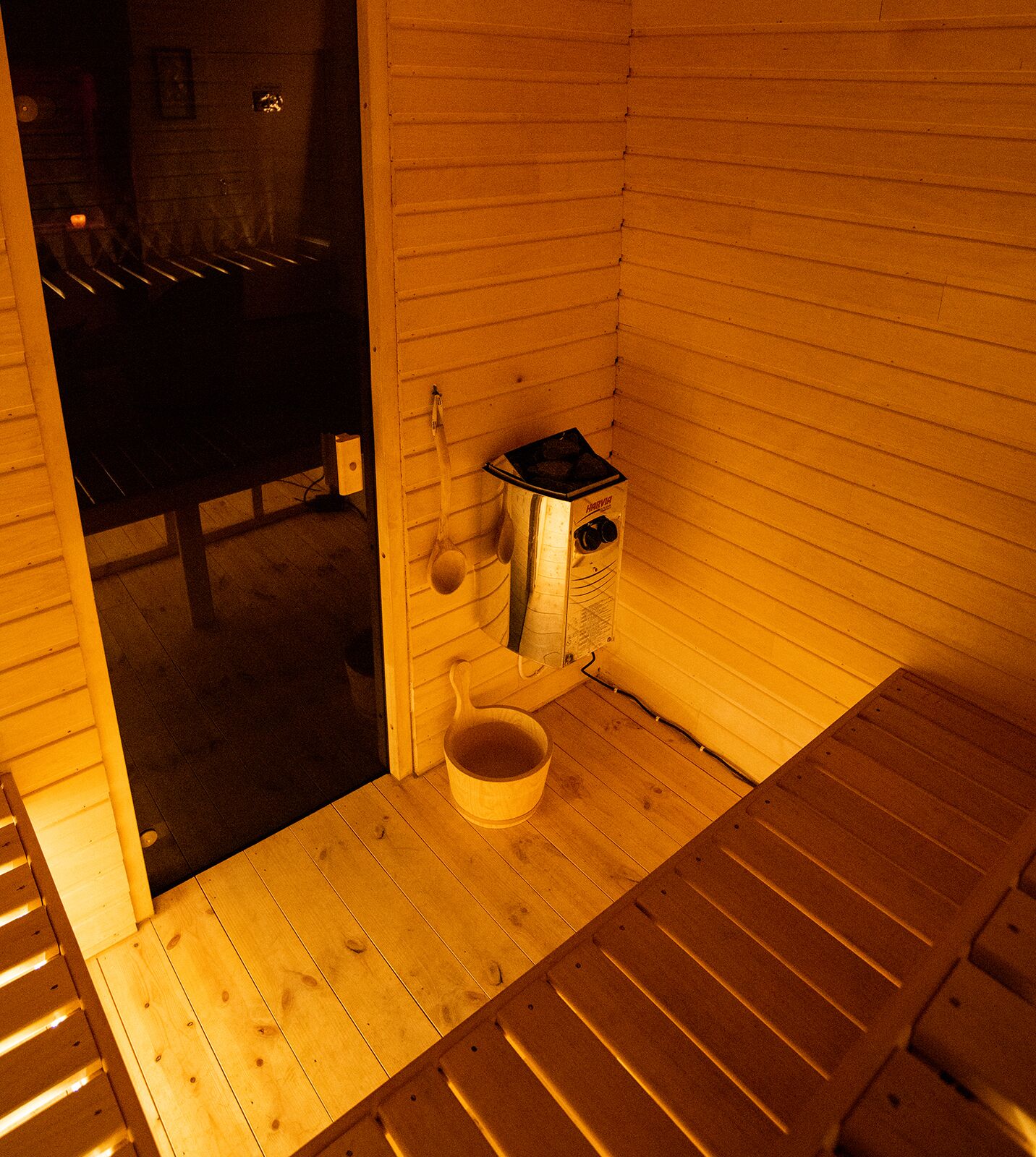 Un sauna avec des bancs en bois, un petit radiateur et un seau en bois.