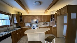 A kitchen with wooden cabinets, a white countertop, a built-in microwave, a sink, and two stools. - Betsy Ross,, Great Downtown,, Residence (Gaylord)