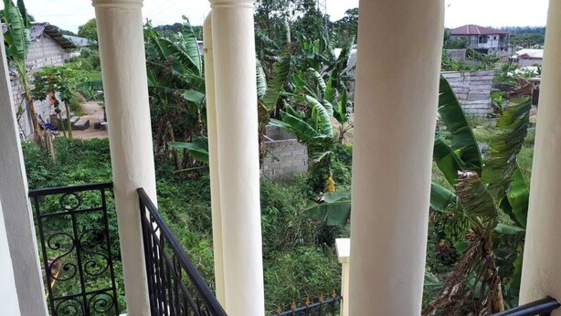 A balcony with white columns and black wrought iron railings overlooking a lush garden with banana trees. - Comfortable duplex / 160 m2 (Douala)