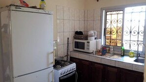A compact kitchen with a refrigerator, stove, microwave, and a window with decorative iron bars. - Comfortable duplex / 160 m2 (Douala)