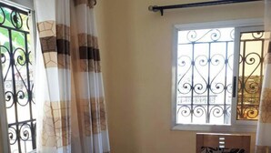 A room with a bed, a window with decorative iron bars, and a curtain with a geometric pattern. - Comfortable duplex / 160 m2 (Douala)