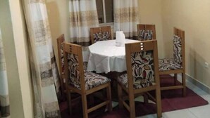A dining area with a round table and four chairs, a window with curtains, and a ceiling light fixture. - Comfortable duplex / 160 m2 (Douala)