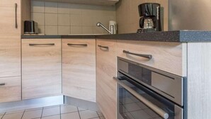 Une cuisine moderne avec des meubles en bois clair, des appareils électroménagers en acier inoxydable et un sol carrelé.