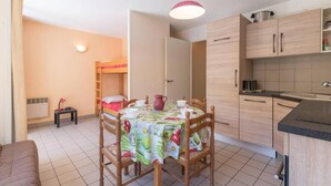 Un espace de vie compact comprenant un lit superposé, une table à manger pour deux personnes et un coin cuisine.