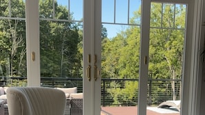 A room with a round marble table, a chair, and a view through large glass doors to an outdoor area with a patio and trees. - Elegant & Private Sparta Home – Pool, Deck, and Luxury Comfort (Sparta)