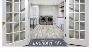 A laundry facility with two washing machines, a drying machine, and a small table. - Elegant & Private Sparta Home – Pool, Deck, and Luxury Comfort (Sparta)