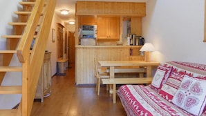 Ein gemütliches Blockhaus-Interieur mit einer Holztreppe, einem Essbereich, einer Küchenzeile und einer Couch mit gemusterten Kissen.