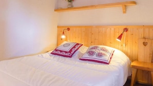 Ein Bett mit weißer Bettwäsche, zwei Kissen mit Herzmuster, ein hölzernes Kopfende und ein Regal mit einer Blumenvase.