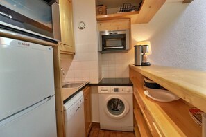 Una cocina compacta con un refrigerador Bosch, lavadora, microondas y un lavamanos.