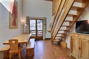 Una mesa de comedor de madera con bancos, un televisor sobre un mueble de madera y una escalera.