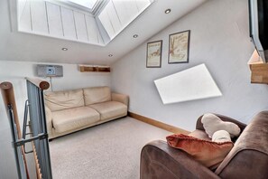 A compact living space with a high ceiling, a sofa, a brown armchair, a radiator, and two framed pictures on the wall.