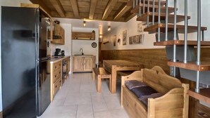 A compact kitchen with wooden cabinets, a black refrigerator, and a wooden bench with a cushion.
