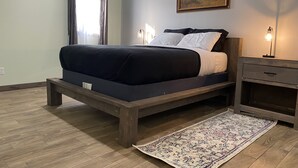 Een slaapkamer met een bed, nachtkastje, lamp, schilderij en een raam met gordijnen.