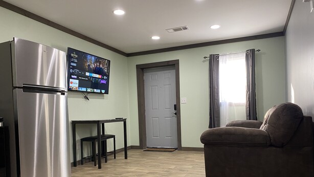 Een knus verblijf met een kitchenette, een flatscreen-televisie aan de muur, een bank en een deur naar een andere kamer.