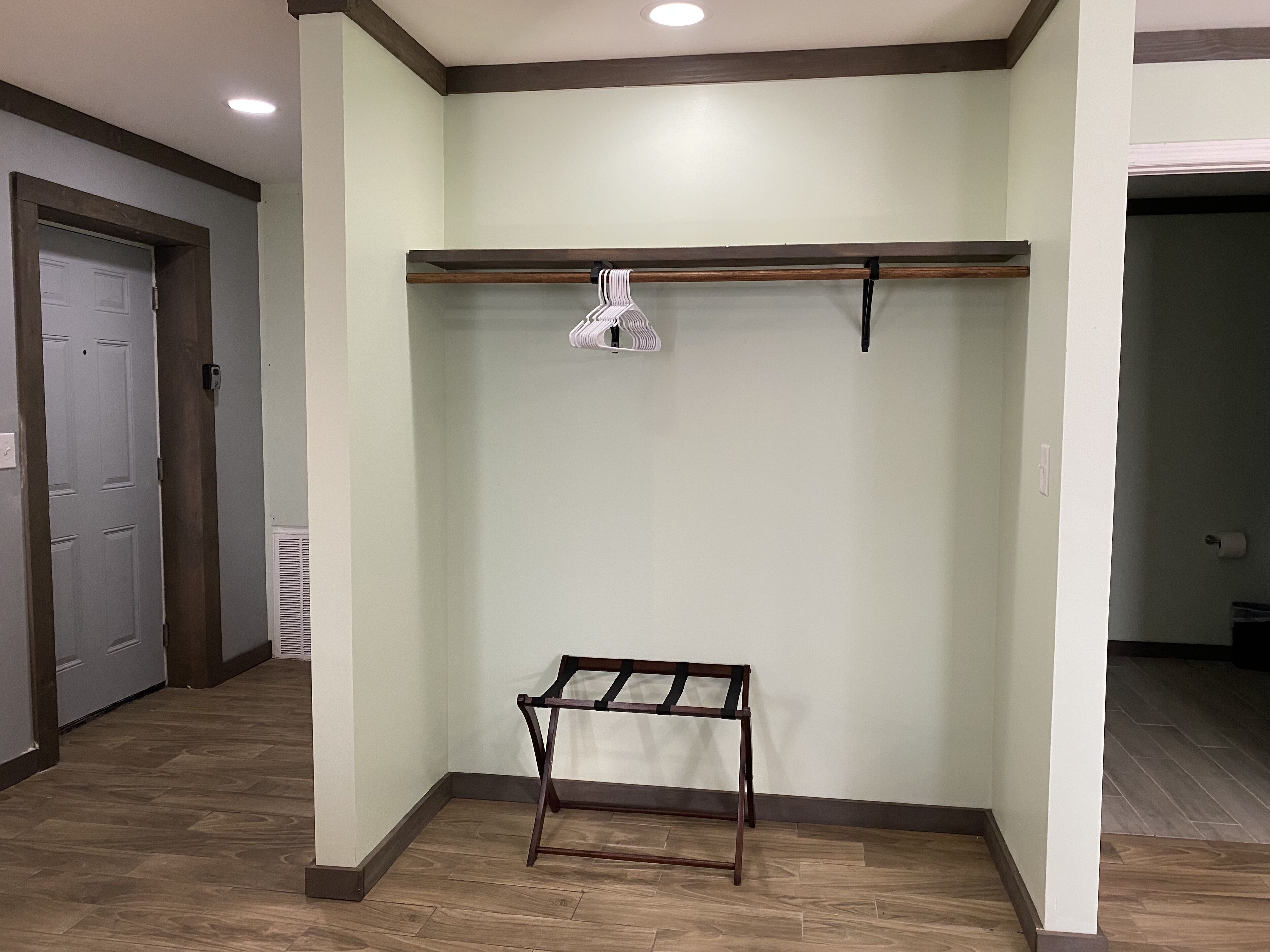 Un armario vestidor con un banco de madera, una barra para colgar ropa y una puerta.