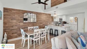 Una cocina moderna con armarios blancos, una isla central y un comedor con sillas blancas.