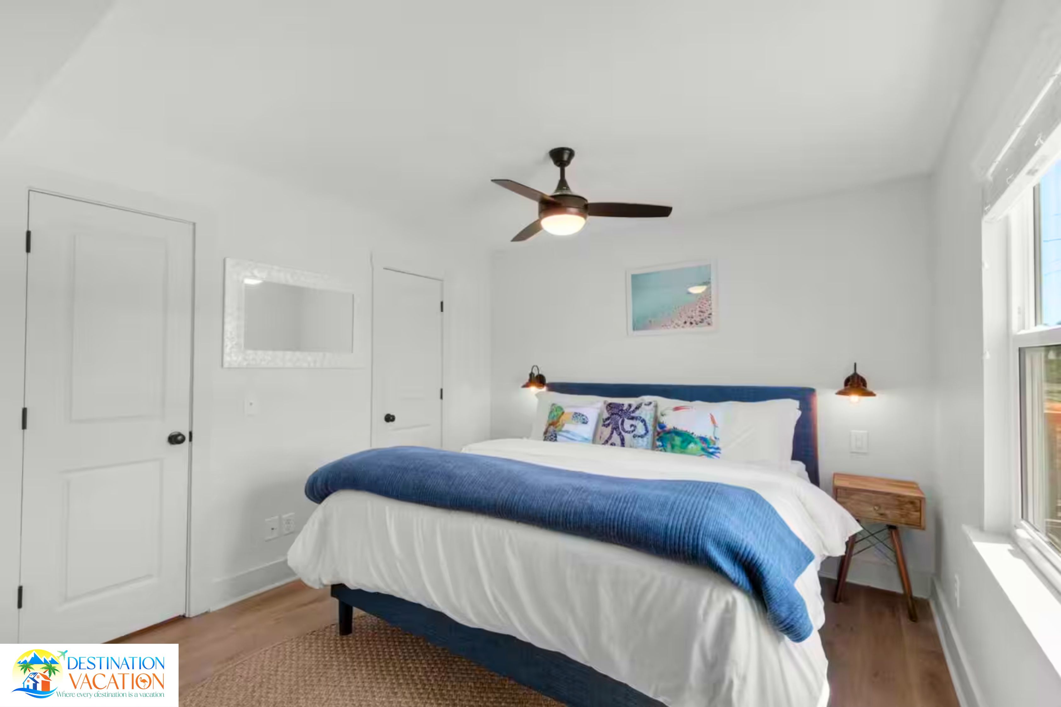Un dormitorio con una cama, ventilador de techo, ventana y mesita de noche.