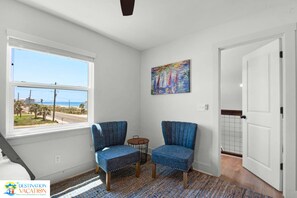 Una habitación con un ventanal grande, dos sillas, una mesita y un cuadro de colores en la pared.