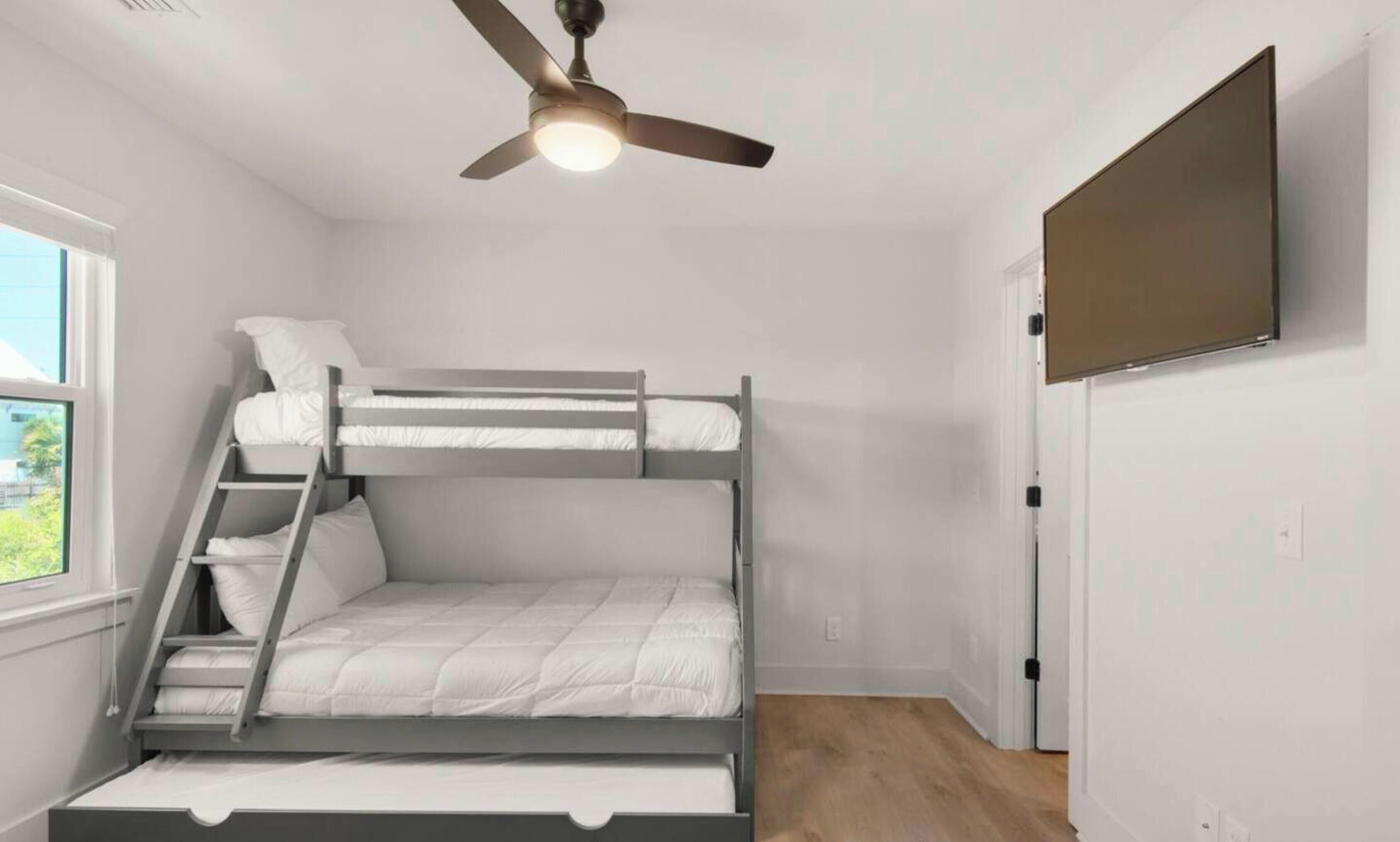 Een slaapkamer met een stapelbed, een plafondventilator, een raam en een deur.