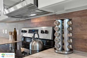 Una cocina moderna con estufa de acero inoxidable, hervidor y un original especiero.