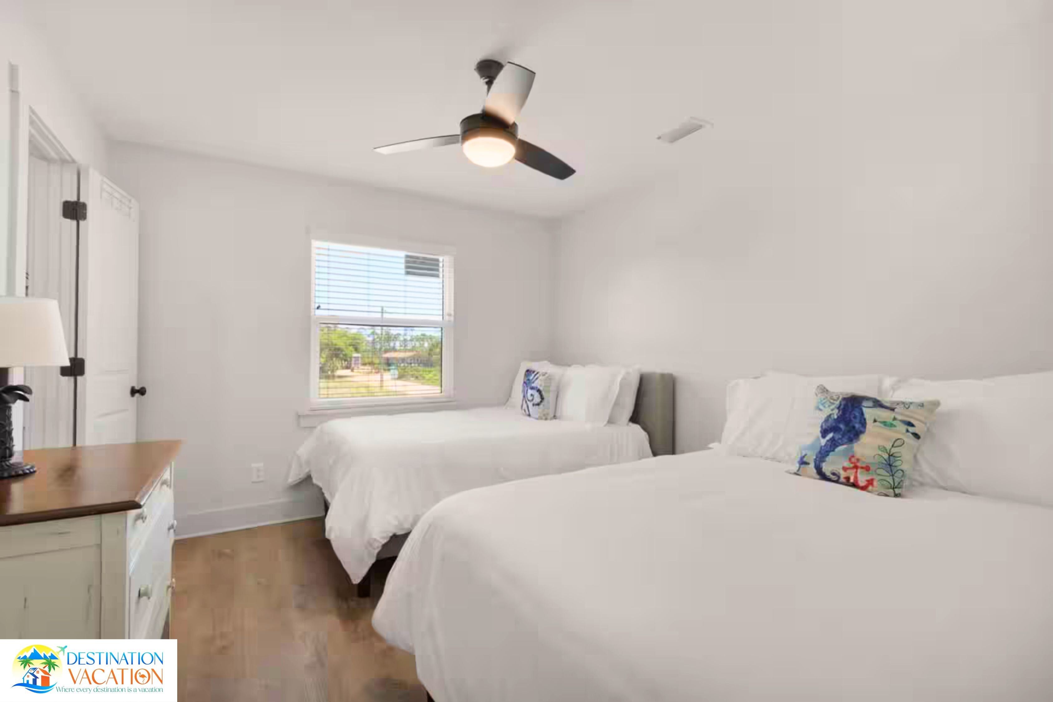 Un dormitorio con dos camas, un ventilador de techo, una ventana con persianas y suelo de madera.