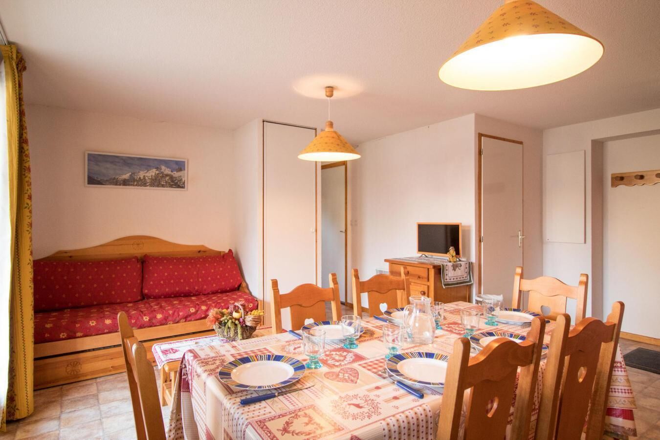 Une pièce chaleureuse avec une table à manger dressée pour quatre personnes, un canapé en bois et un téléviseur dans un coin.