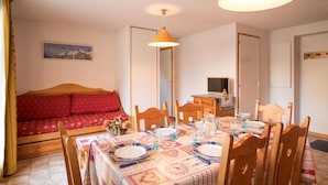 A cozy room with a dining table set for four, a wooden sofa, and a television in the corner.