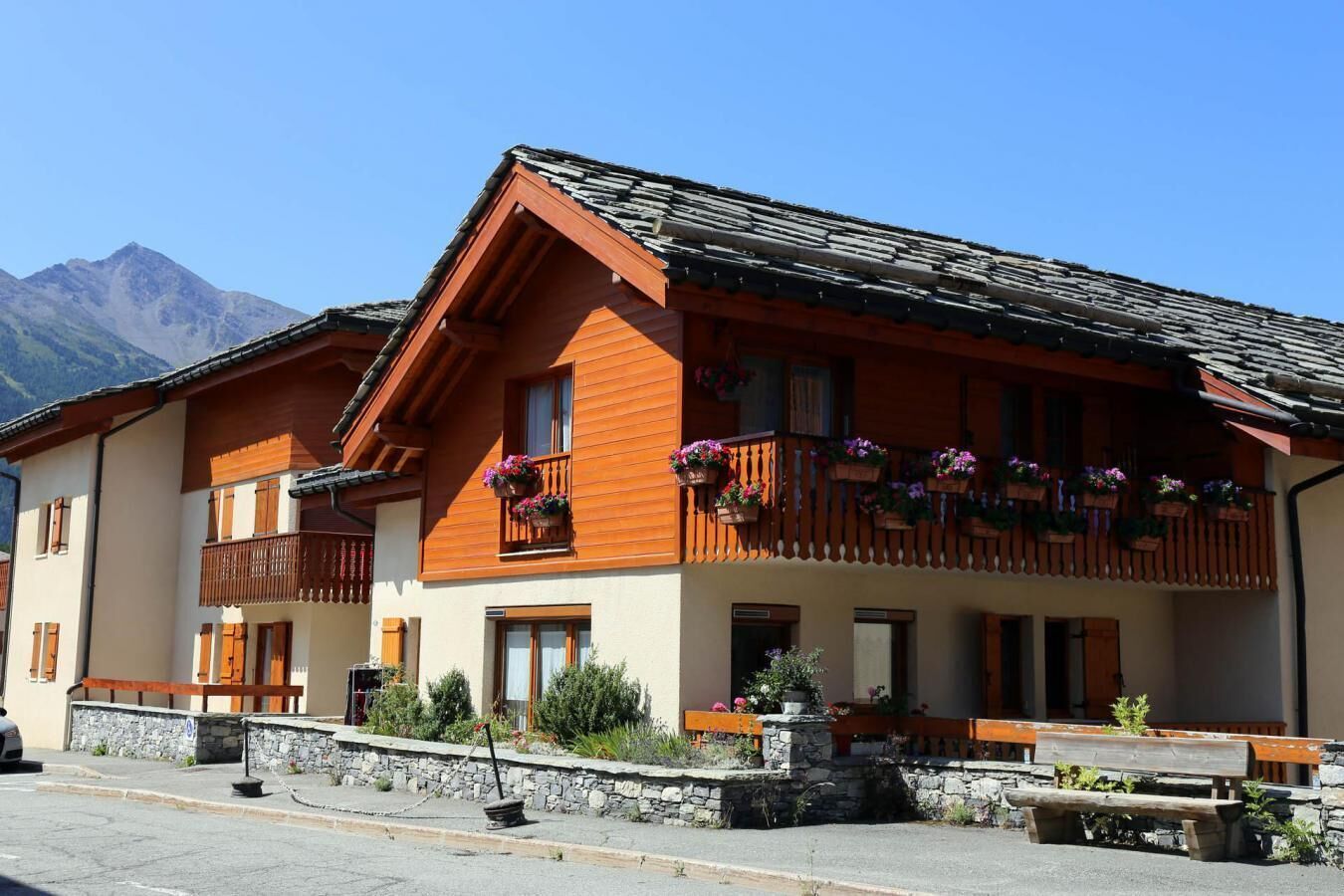 A traditional chalet with wooden balconies, stone steps, and a mountain backdrop.