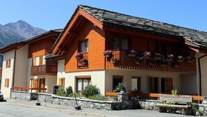 A traditional chalet with wooden balconies, stone steps, and a mountain backdrop.