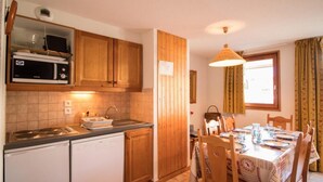 A compact kitchen with wooden cabinets, a microwave, a sink, and a dining area with a table set for four.