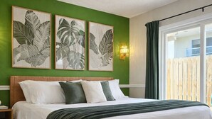 Ein Bett mit einem gewobenen Kopfteil, einer grünen Wand und drei gerahmten Kunstwerken mit Blättern.