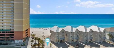 A beachfront hotel with multiple-story buildings, a parking lot, and a clear view of the ocean.