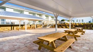 Ein Außenbereich mit einer Holzterrasse, Picknicktischen und einem überdachten Sitzbereich.
