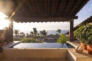 Piscina no terraço com vista para o oceano e palmeiras.