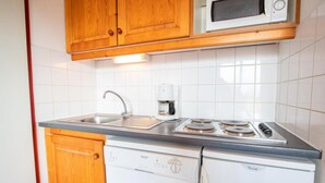 Une cuisine compacte dotée de meubles en bois, d’un évier en acier inoxydable, d’une machine à café, d’un four à micro-ondes et d’un lave-vaisselle encastré.