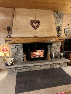 A stone fireplace with a heart-shaped decoration above it, a wooden mantel, and a stone wall on the right.