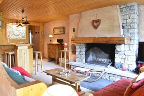 A cozy living room with a stone fireplace, wooden furniture, and a television mounted on the wall.