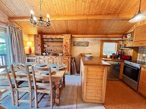 A wooden cabin interior with a dining area, kitchen, and a chandelier.