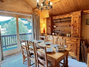 A wooden dining table with chairs, a chandelier, and a view of a mountainous landscape through a sliding door.