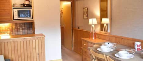 A compact kitchen with a microwave, a wooden cabinet, and a dining area with a table set for two.