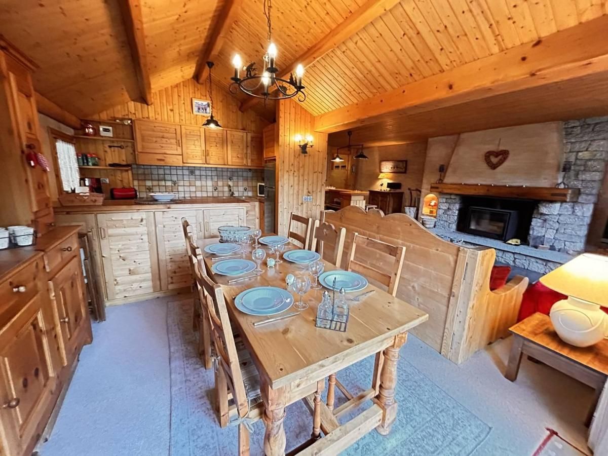 A wooden interior with a dining table set for six, wooden cabinets, a stone fireplace, and a chandelier.