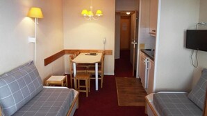 Una habitación compacta con sofá, una mesita, comedor y kitchenette.