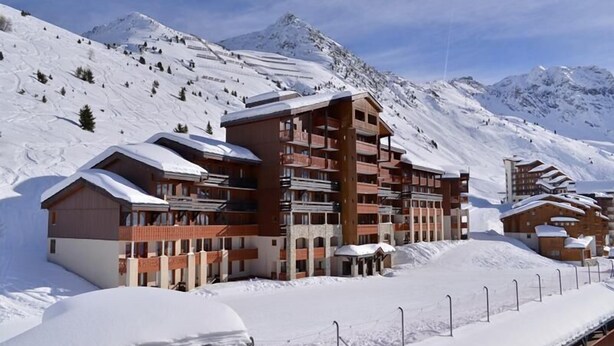Un complejo turístico en la montaña cubierto de nieve, con edificios de varios pisos, pistas de esquí y un cielo despejado.