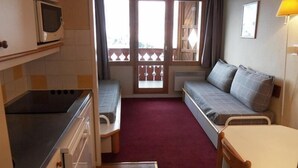Una habitación compacta con kitchenette, sofá cama, mesa de comedor y vistas al exterior.