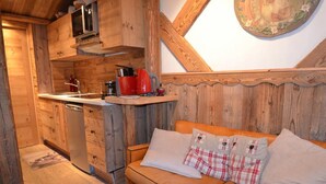 A cozy cabin interior with a wooden kitchen, a sofa with plaid cushions, and a decorative wall piece. - 10m from ski slopes, 7th floor, tv, 24m², Les Menuires (Les Menuires)
