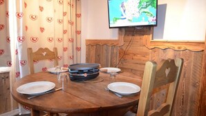 A dining area with a round wooden table, four chairs, a television mounted on the wall, and heart-patterned curtains. - 10m from ski slopes, 7th floor, tv, 24m², Les Menuires (Les Menuires)