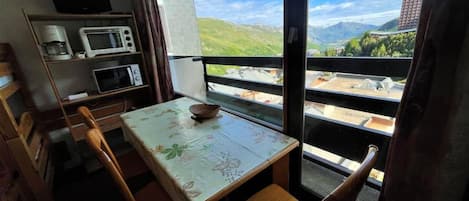 Un pequeño comedor con mesa y sillas, un microondas, una cafetera y vistas a un paisaje montañoso.
